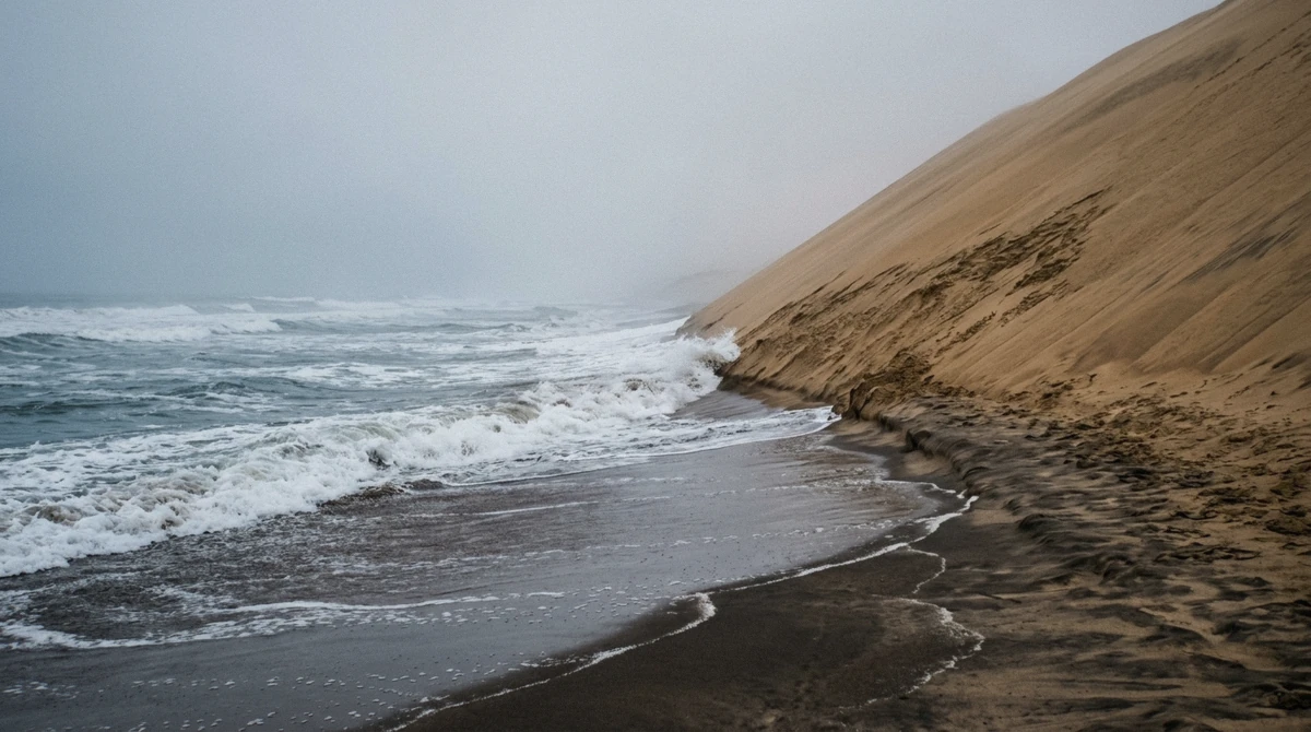Waves washing the base of a tall dune on the Sandwich Harbour beach with a low tide line in Namibia